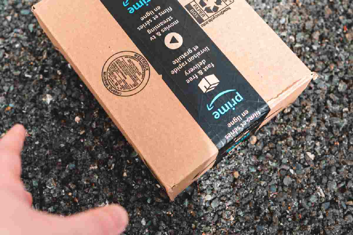 Scatola di Amazon Prime per terra con una mano sfocata che fa per raccoglierla