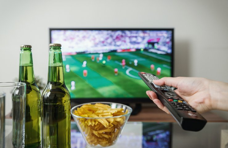 Due birre e delle patatine su un tavolino da tv con la tv e il calcio nello sfondo