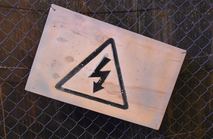 Ad una rete da cantiere è attaccato un cartello sbiadito con il triangolo di attenzione scariche elettriche