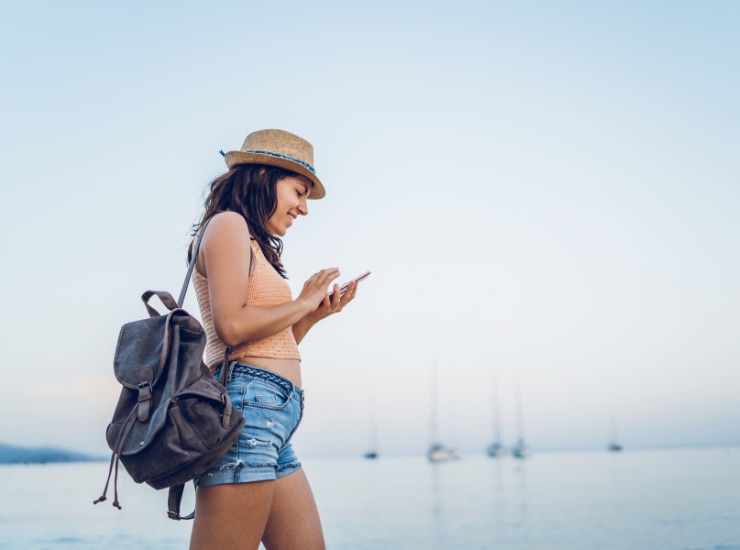 Ragazza cammina in riva la mare guardando il suo cellulare