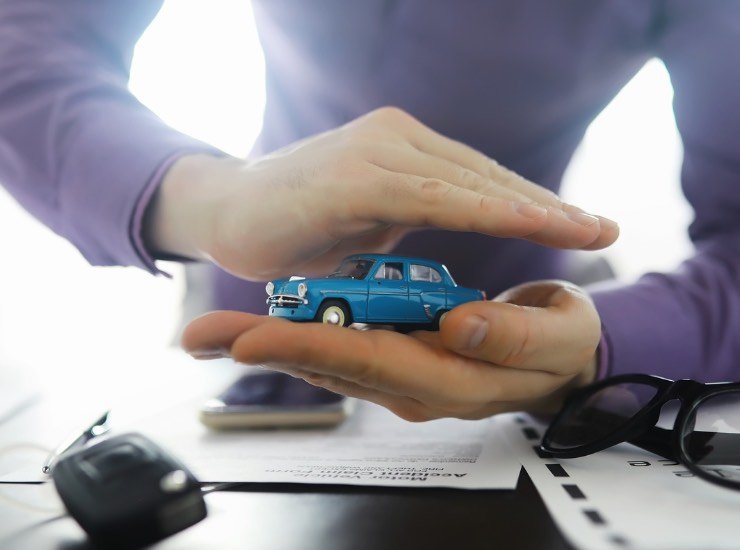 un uomo protegge con le mani un modellino di auto vintage azzurra