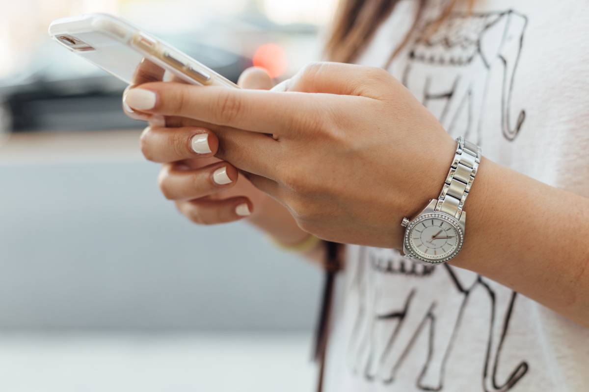 Mani di una ragazza che tengono un cellulare bianco